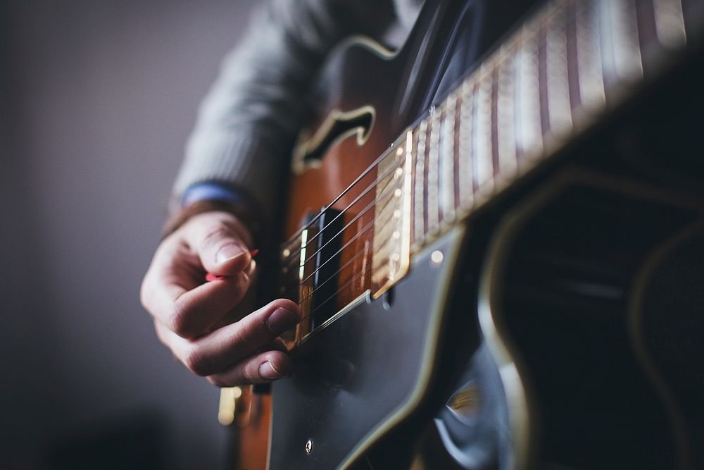 A close-up of a person's hand with a pick playing a guitar. Original public domain image from Wikimedia Commons